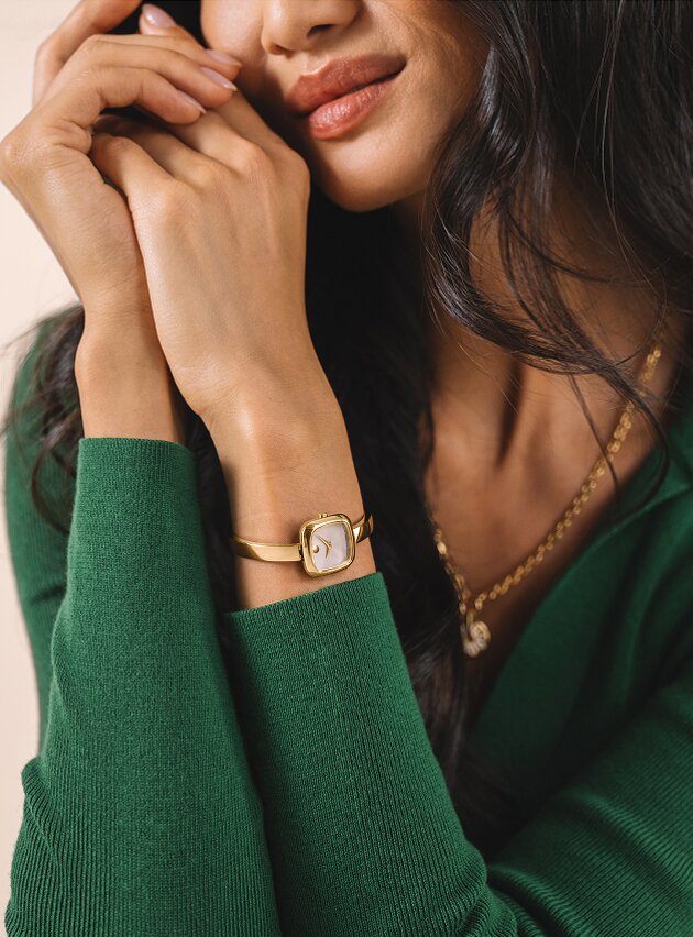 Woman in a green sweater wearing the gold tone Museum Bangle Square watch.