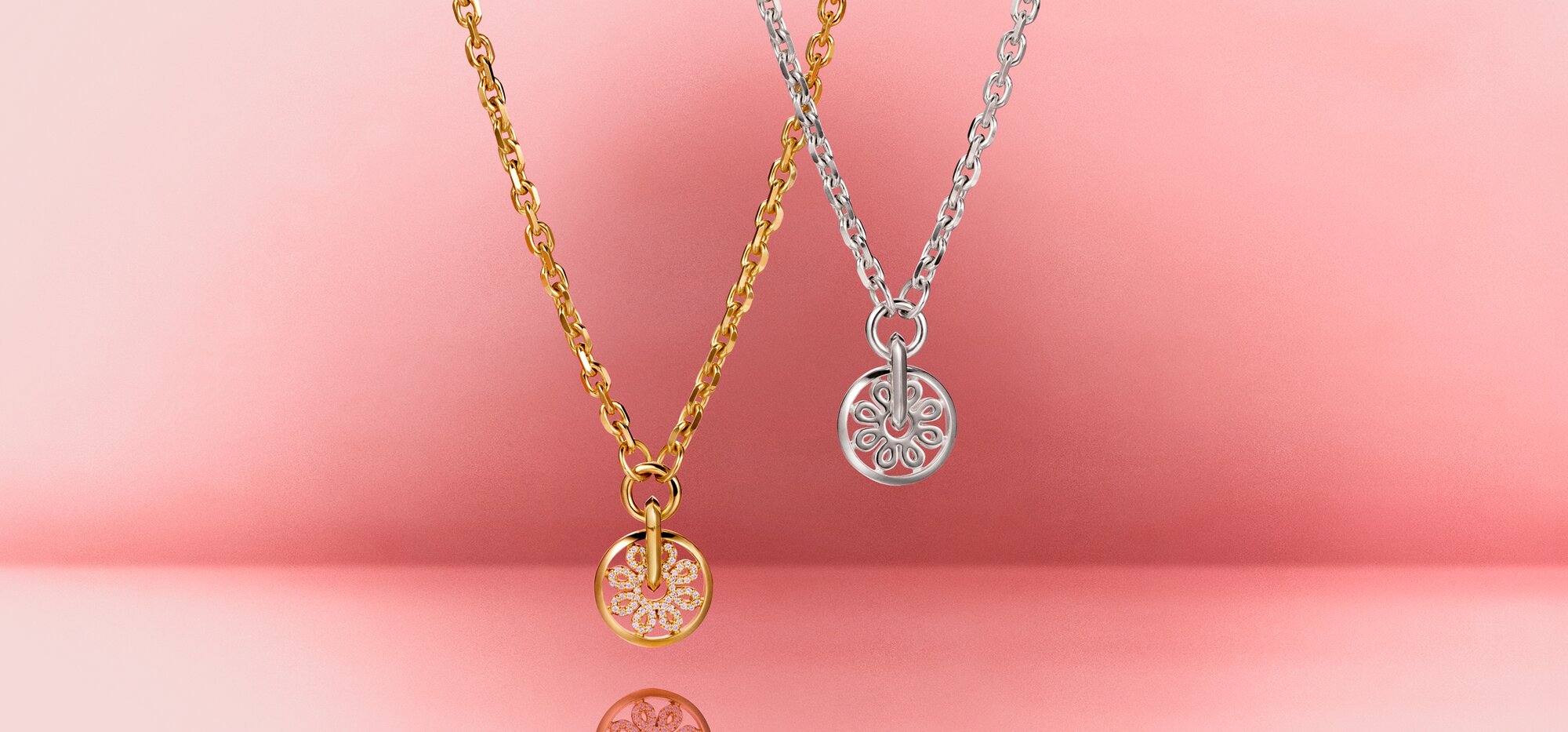 Gold tone Fleur necklace with lab grown diamonds hanging next to a silver Fleur necklace in front of a pink backdrop 