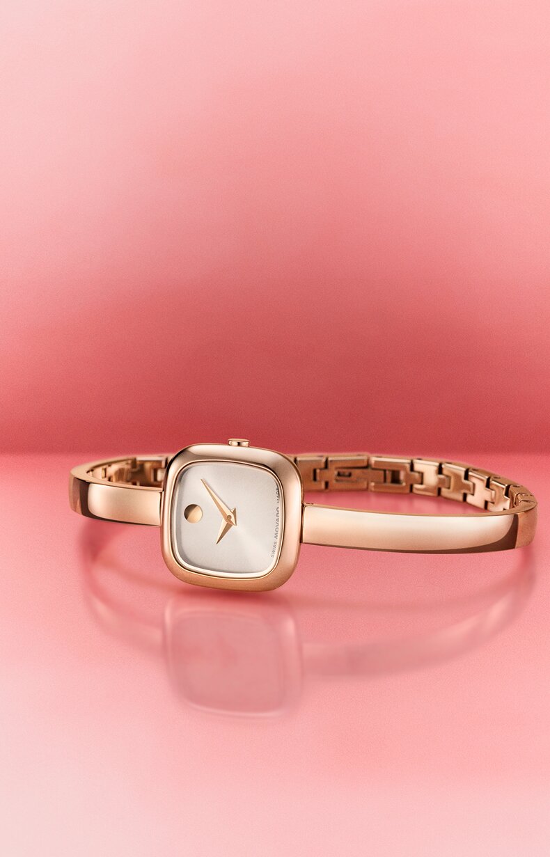Square Museum Bangle watch laying on its side with a pink background.