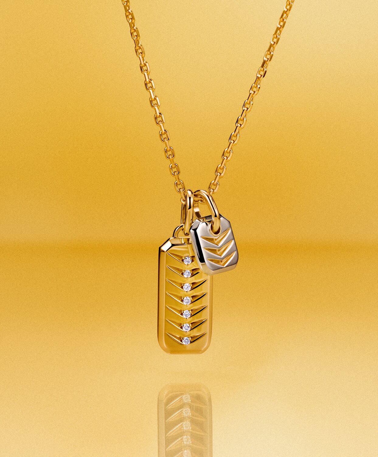 Gold tone women's necklace with a gold tone rectangle chevron charm and silver square charm in front of a yellow background