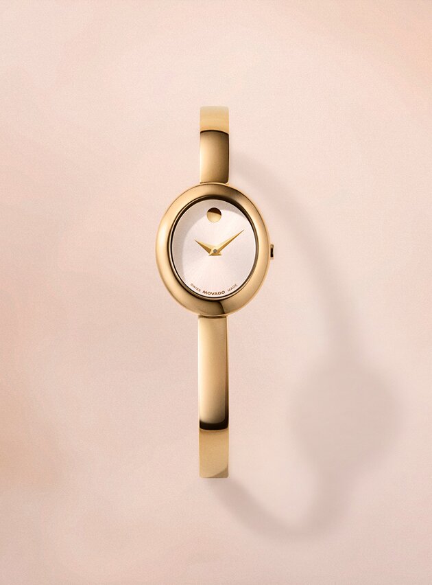 Gold tone Museum Bangle watch with white dial in front of tan background