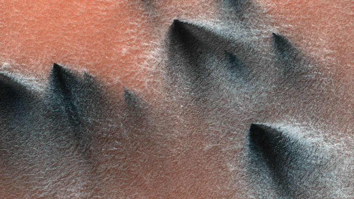 An aerial photo showing gray and black clouds of dust over the surface of Mars