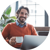 Smiling man with coffee cup in front of computer