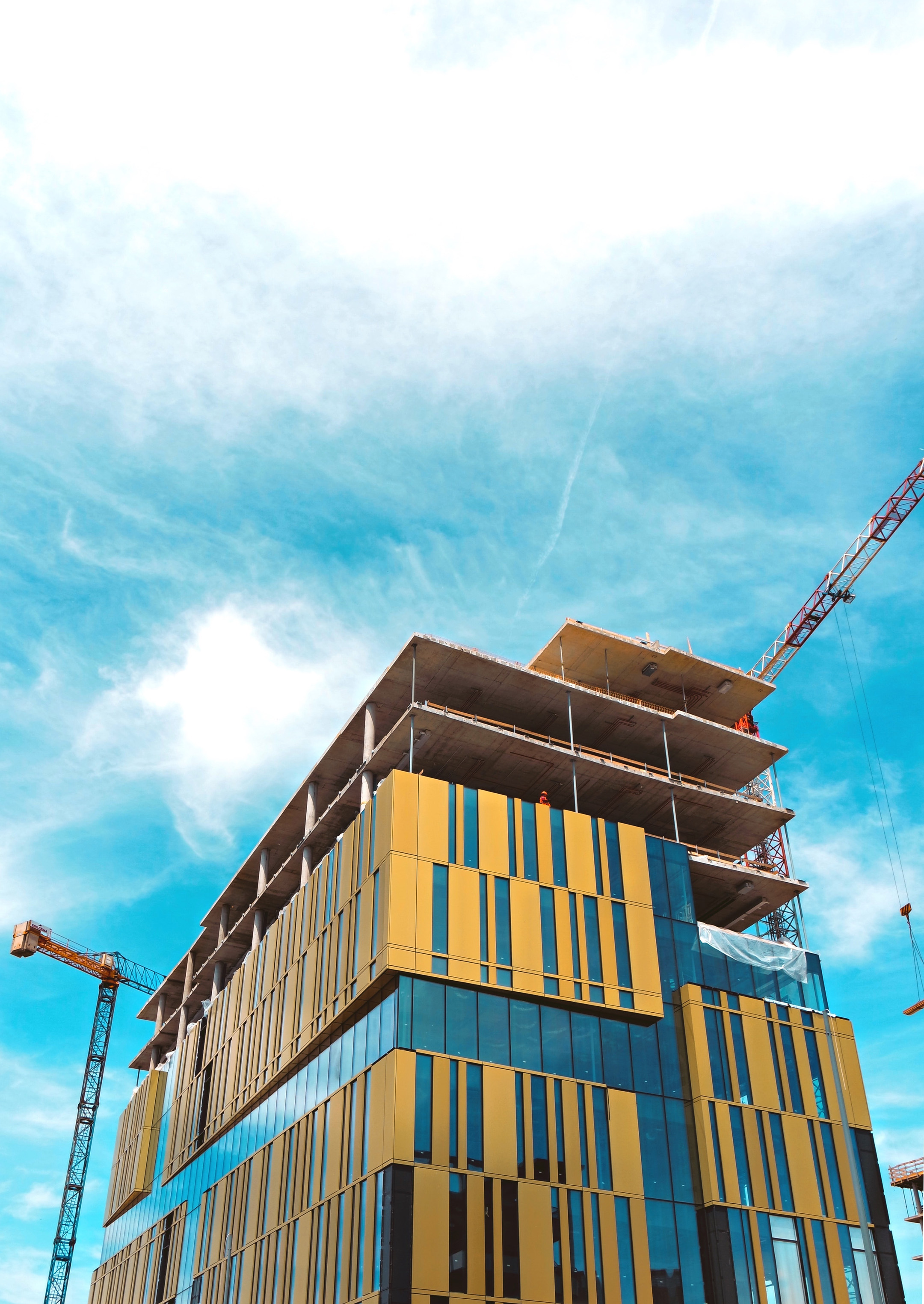 The top of a large skyrise building under construction, shot from a low angle point of view. The sky is clear with a few clouds in the background.