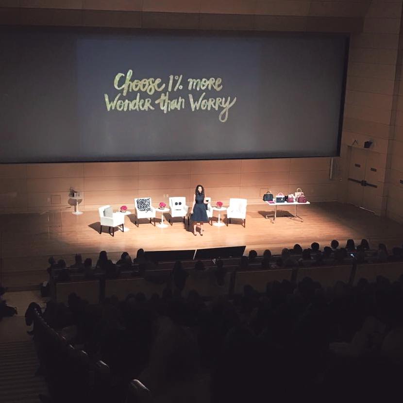 A woman standing in front of a screen that says "Choose 12 more wonder than worry".