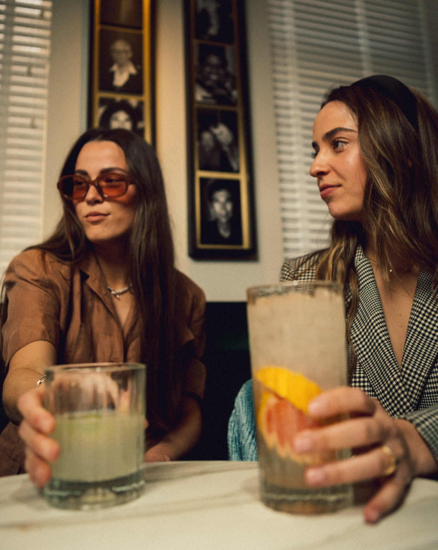 two woman sitting next to each other while holding cocktails