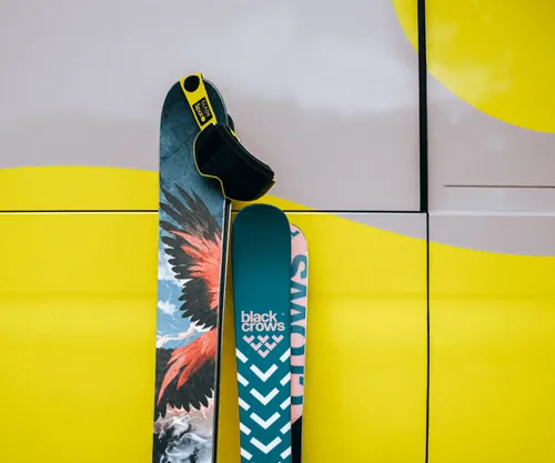Two colorful skis leaning against a yellow and gray vehicle.