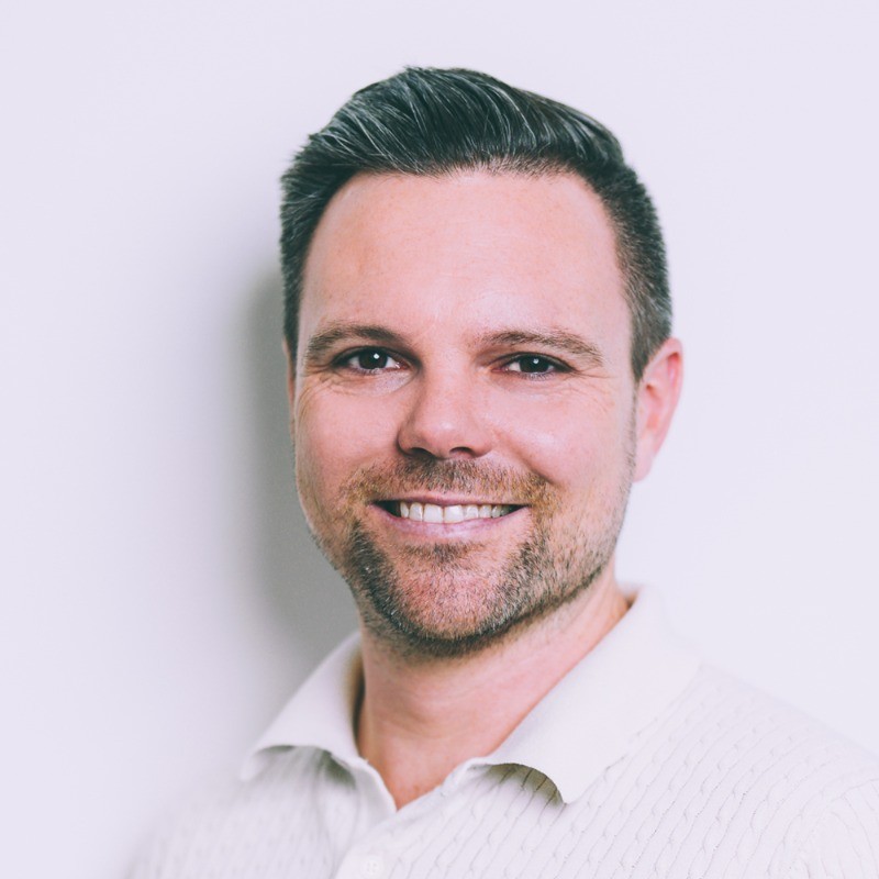 Portrait of a smiling man with short hair and a beard against a white background.
