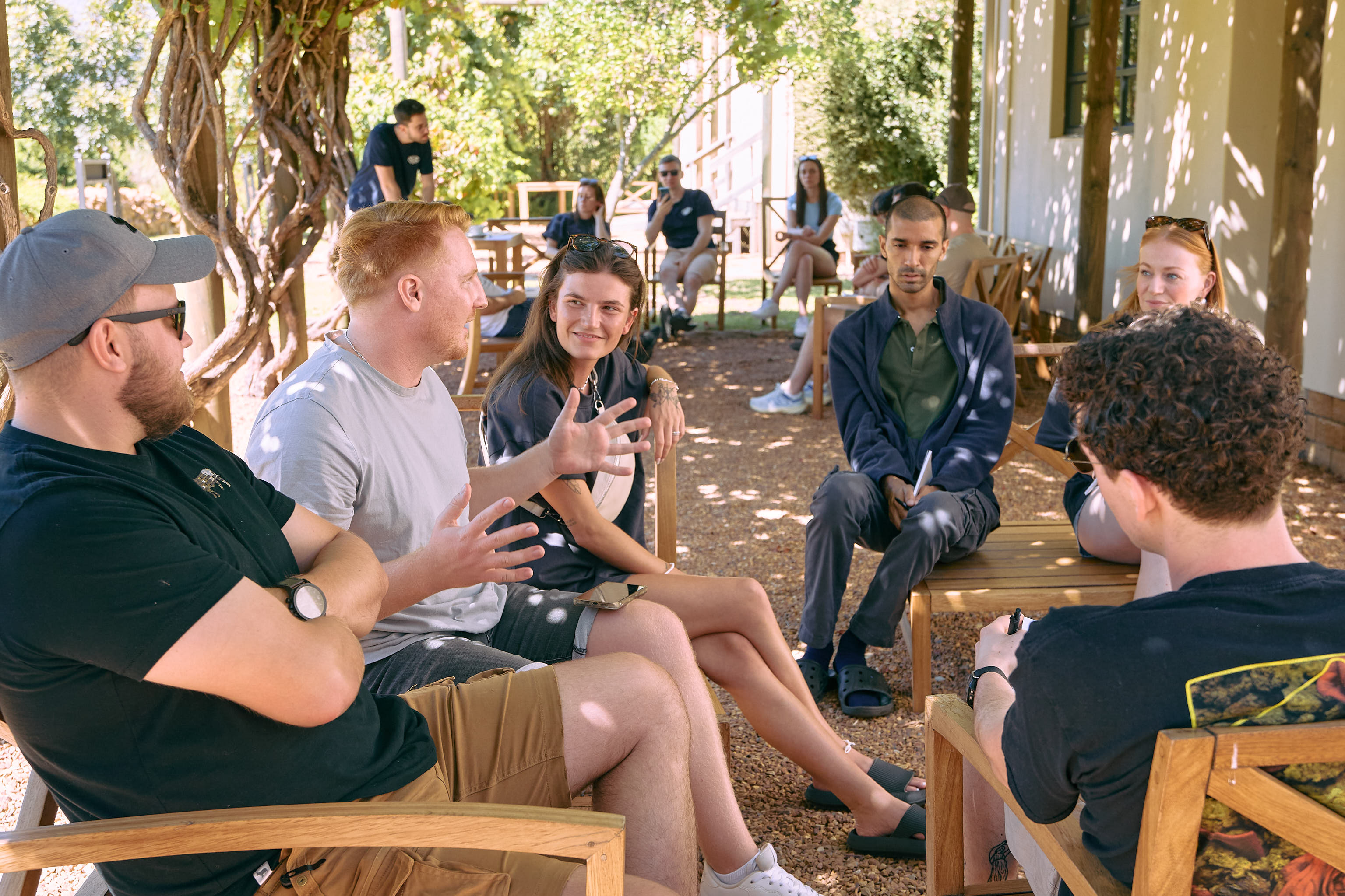 A group of people is sitting outside on chairs, chatting in a relaxed setting.