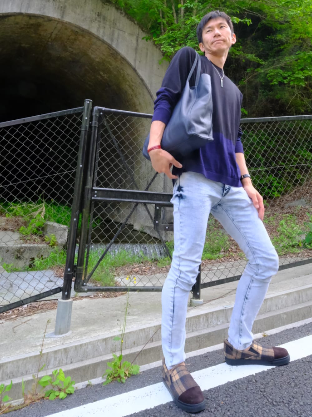 ブルー系のデニムパンツ、ブラック系のニット/セーター、ブルー系のトートバッグを着用したメンズの春コーディネートの1枚目の写真