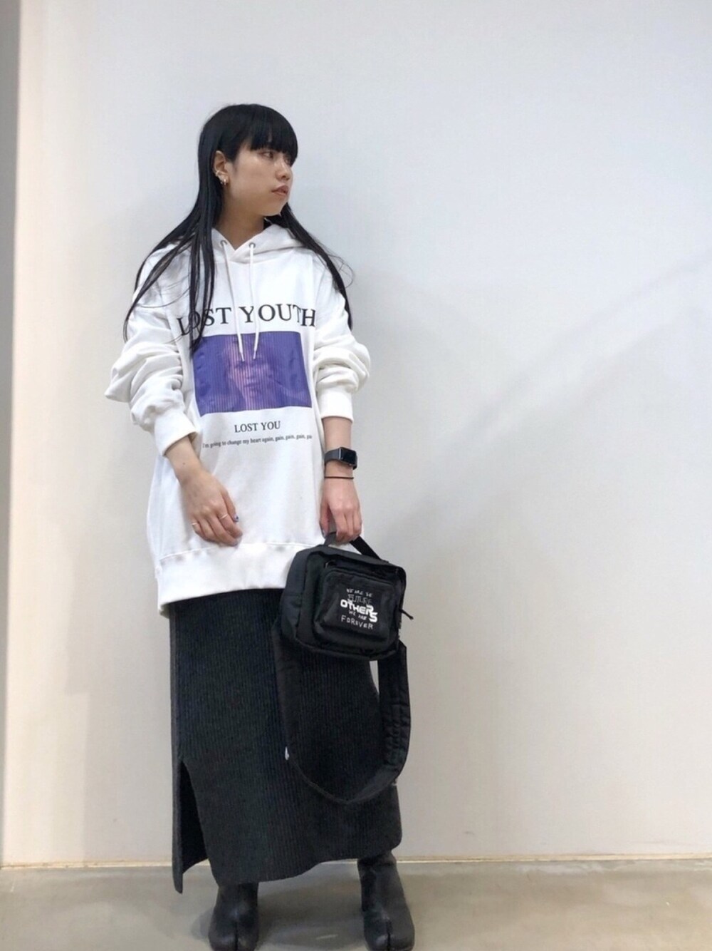 ホワイト系のパーカー、ブラック系のショルダーバッグ、グレー系のスカートを着用したレディースの秋コーディネートの1枚目の写真