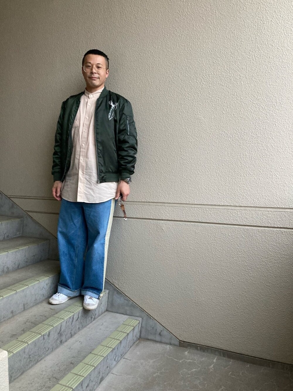 グリーン系のブルゾン、ブルー系のデニムパンツ、ホワイト系のスニーカーを着用したメンズの春コーディネートの1枚目の写真