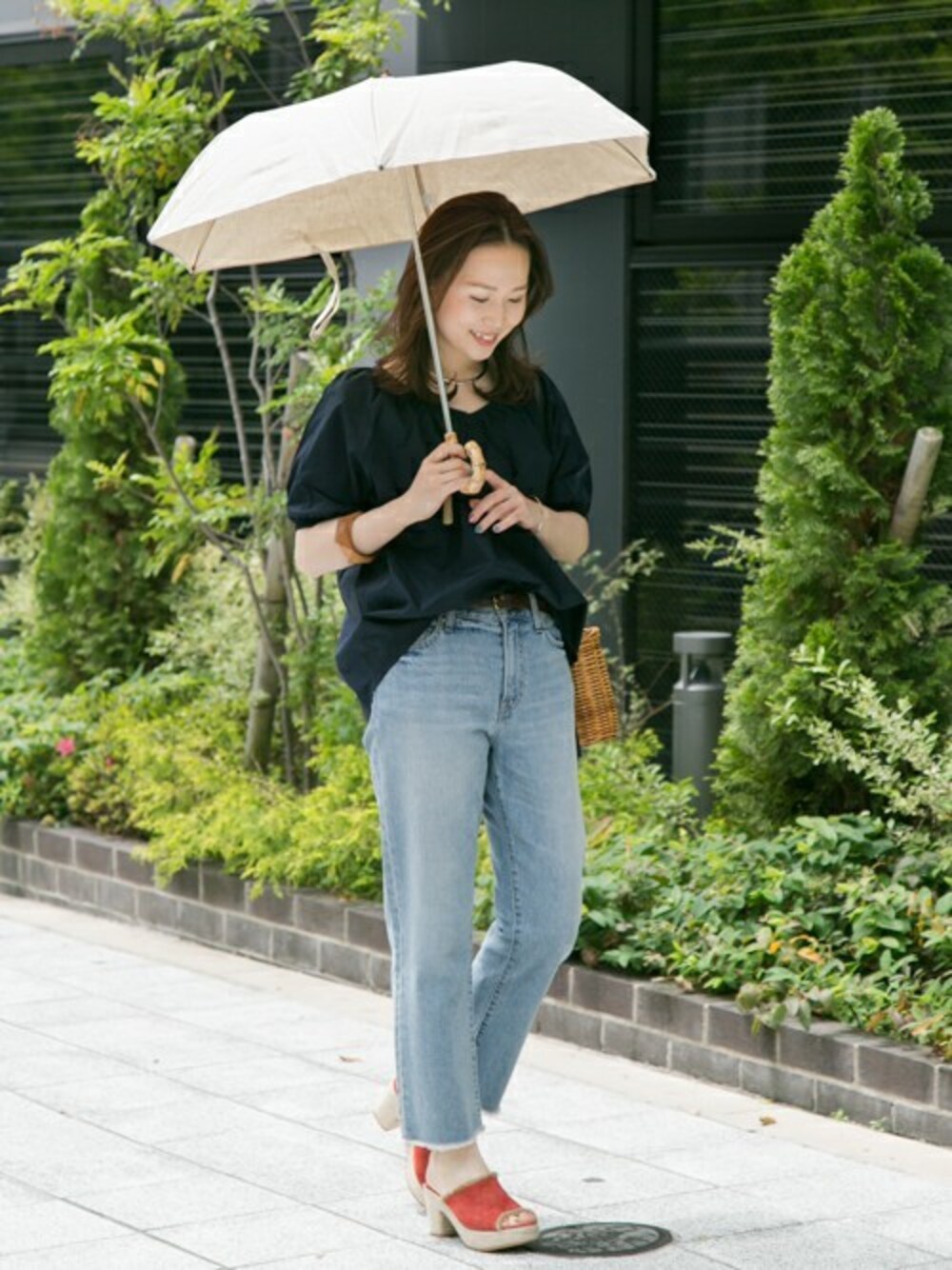 ブルー系のデニムパンツ、ブラック系のかごバッグ、ベージュ系の折りたたみ傘を着用したレディースの春コーディネートの1枚目の写真
