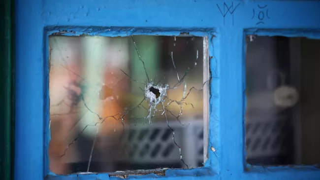 Окно жилого дома, разбитое осколком снаряда, в Донбассе