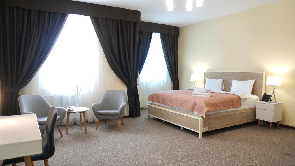 a hotel room with a bed and chairs and windows at ASYR Hotel in Astana