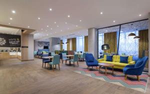 a hotel lobby with a yellow couch and blue chairs at Hampton By Hilton Astana Triumphal Arch in Astana