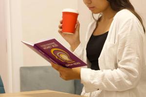 a woman holding a book and a cup of coffee at Five Hotel in Astana