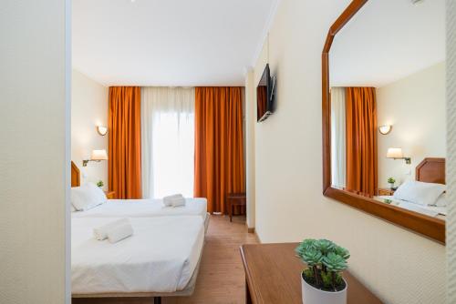 una camera d'albergo con due letti e uno specchio di Hotel Residencial Colibri a Costa da Caparica