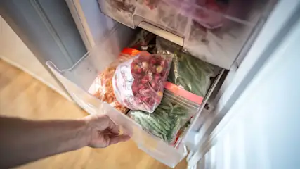 Eine Männerhand öffnet eine Schublade voller gefrorenem Obst und Gemüse von einem Gefrierschrank