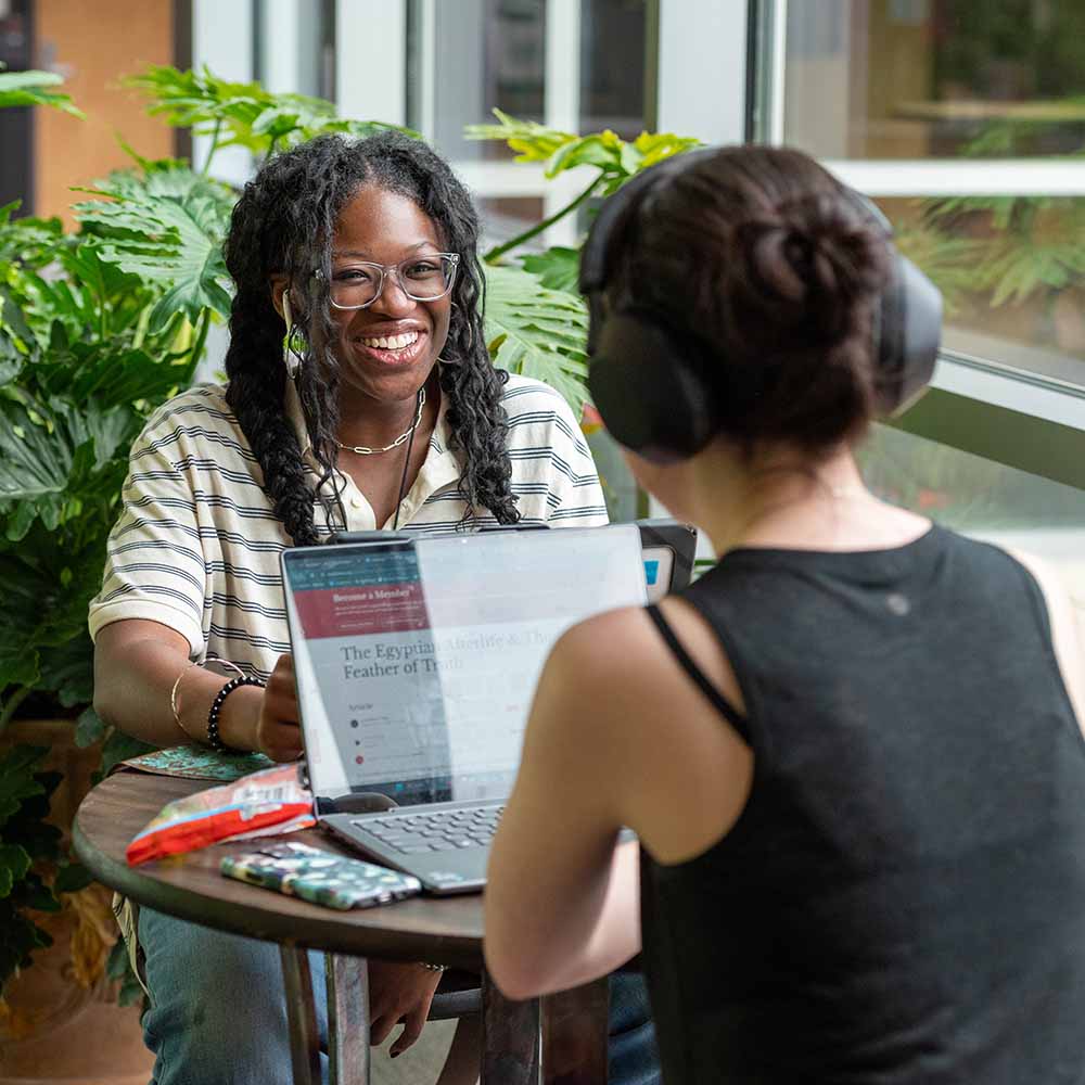 African American student working on laptop talking with another female student