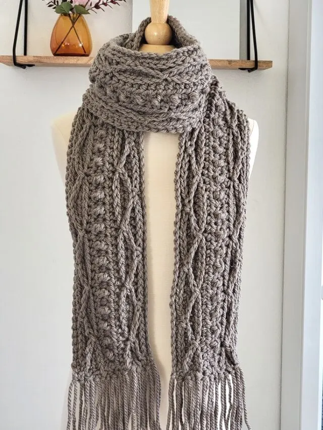Crochet cable scarf pattern finished in Taupe color and displayed on a mannequin