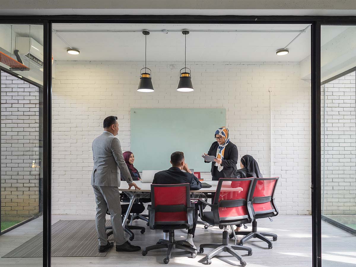 A group of workers sitting around a table in an office with white brick walls and looking at a mobile device