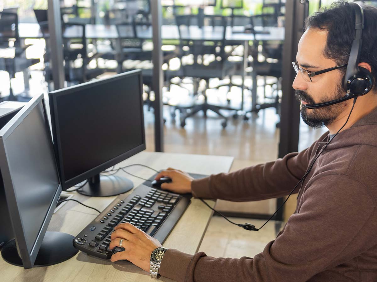 Un uomo con i capelli scuri e la barba che indossa un auricolare e lavora al computer