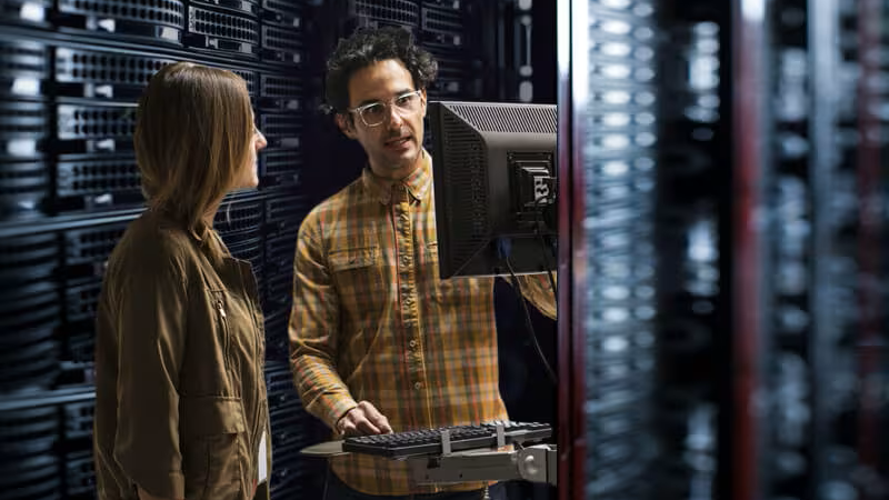 Two individuals looking at a computer in a telco network operations center.