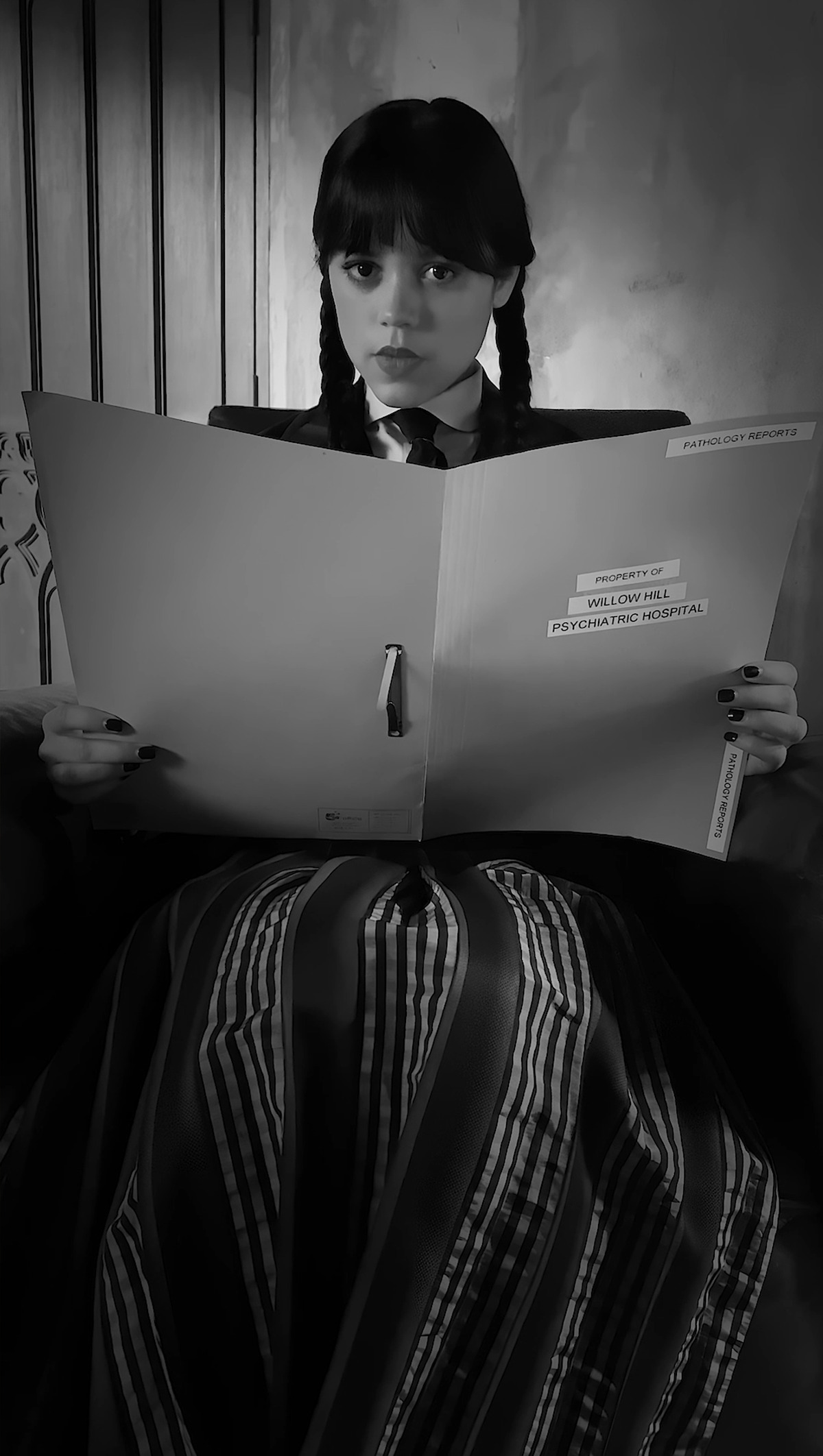 Black and White image of Jenna Ortega as Wednesday Addams reading from a large book