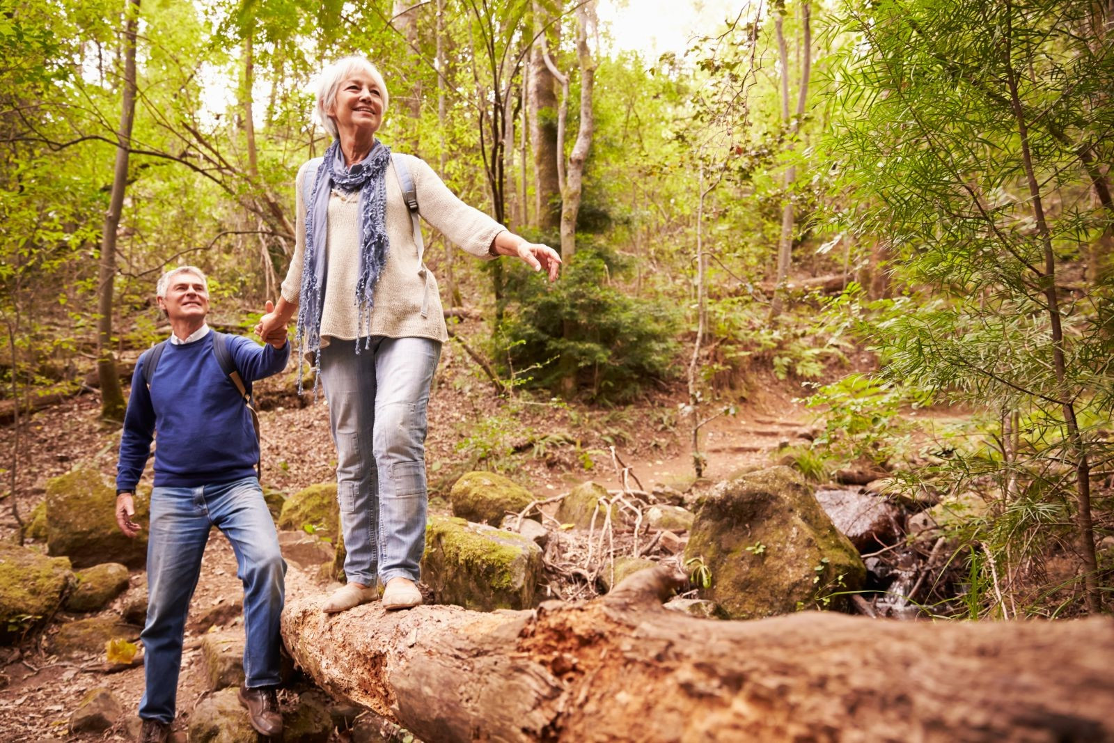 A man and a woman walking on a rock in the woods