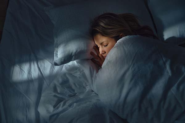 High-angle view of a woman sleeping at night, with a thin line of external light crossing the bed and her face.