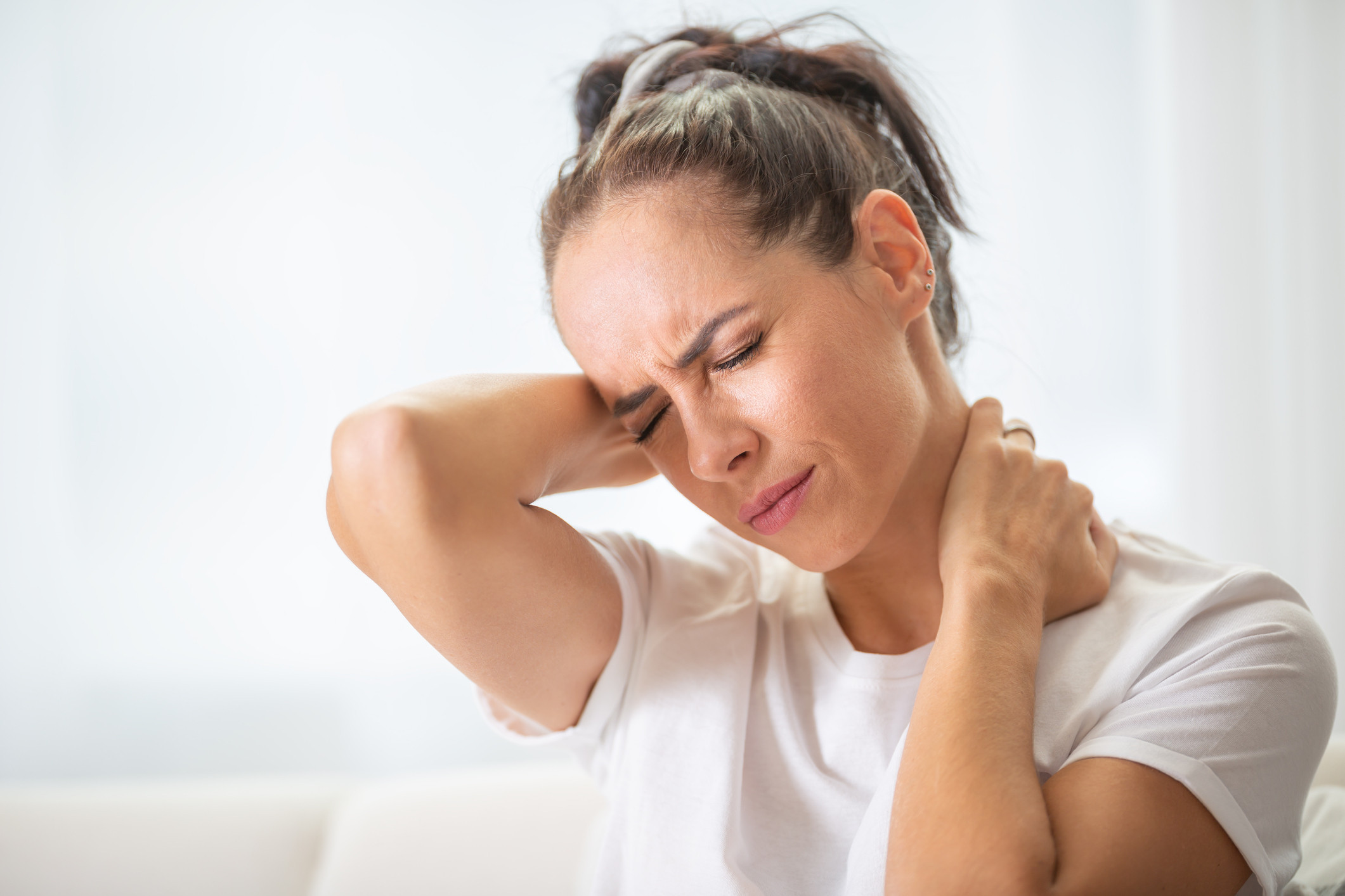 A woman holding her neck in pain while sitting on a couch