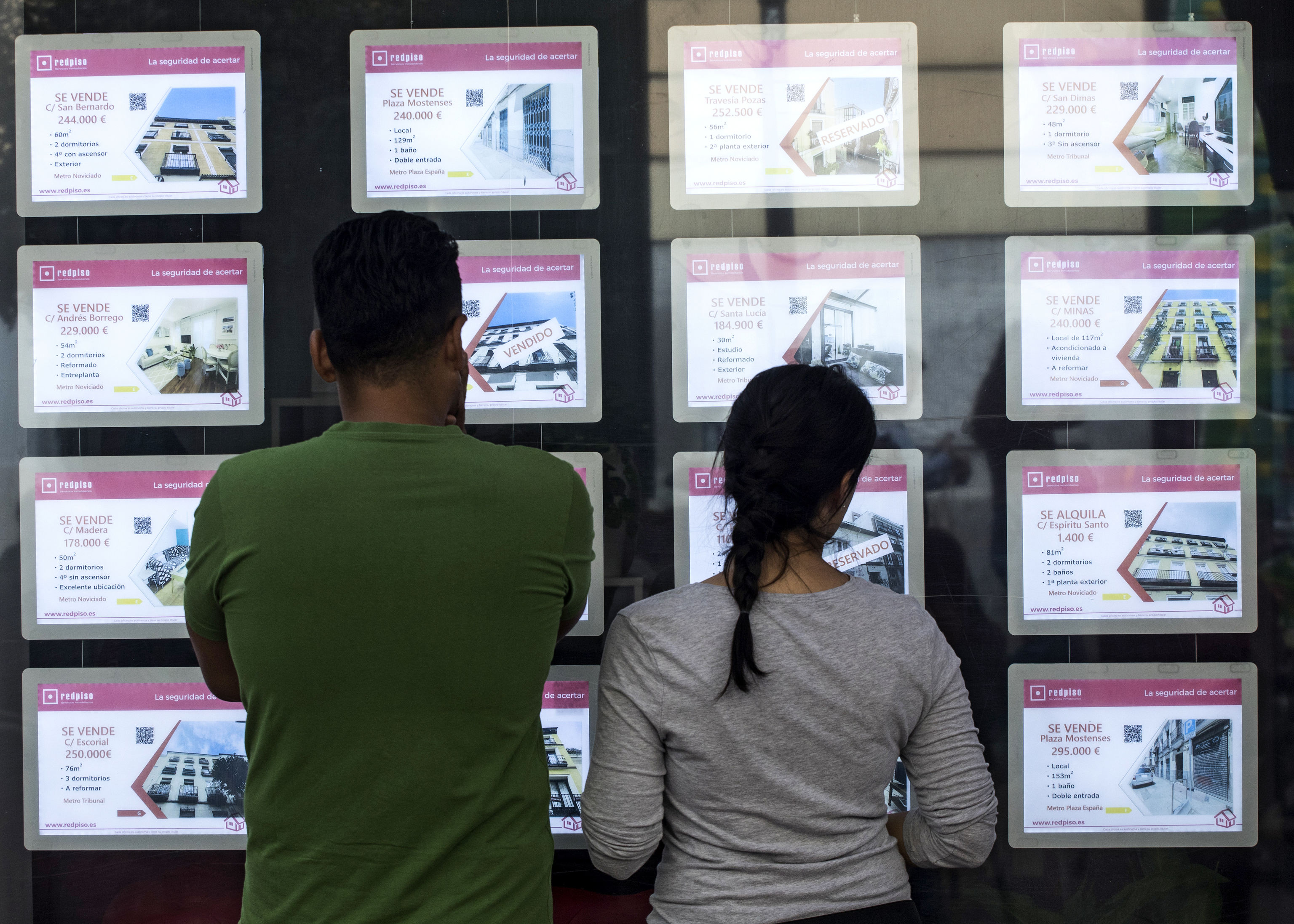 Dos personas miran los anuncios de vivienda en una agencia inmobiliaria.