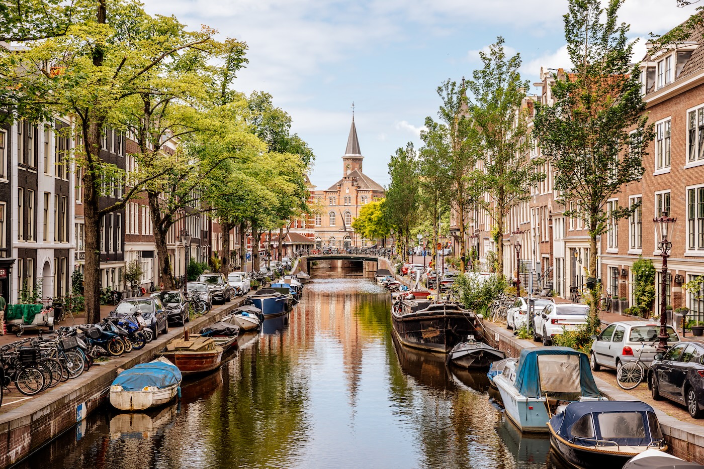 A canal is Amsterdam looks vibrant with bikes and cars parked up either side