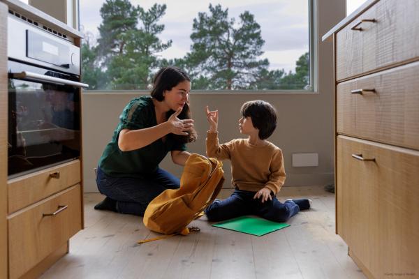 Mother and son communicating through sign language while sitting on floor near kitchen at home