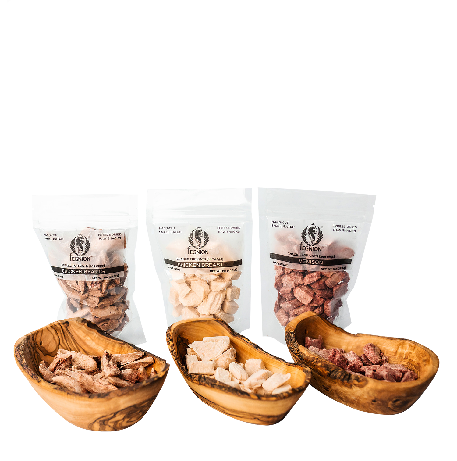 Fegnion-Snacks-new-noHole A studio product shot showing three clear pouches of Fegnion brand freeze-dried raw cat treats: Chicken Hearts, Chicken Breast, and Venison, with corresponding piles of the treats in elegant olive wood bowls.