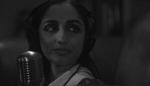 Black-and-white close-up of a women wearing headphones in front of a microphone.