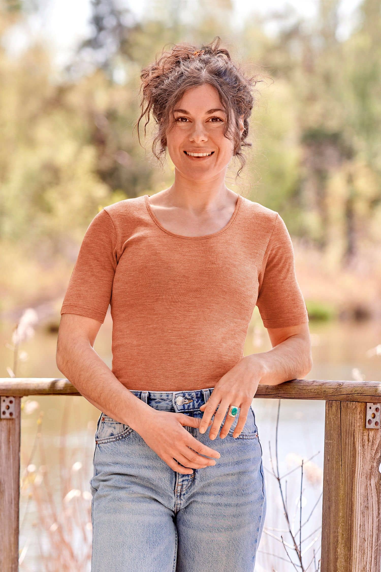 Baumwolle-Wolle-Seide Damen-Kurzarmshirt mit Bio-Fasern Frau mit Jeans lehnt an Geländer und trägt ein oranges Kurzarmshirt aus bio Wolle (kbT), bio Baumwolle (kbA) und Seide