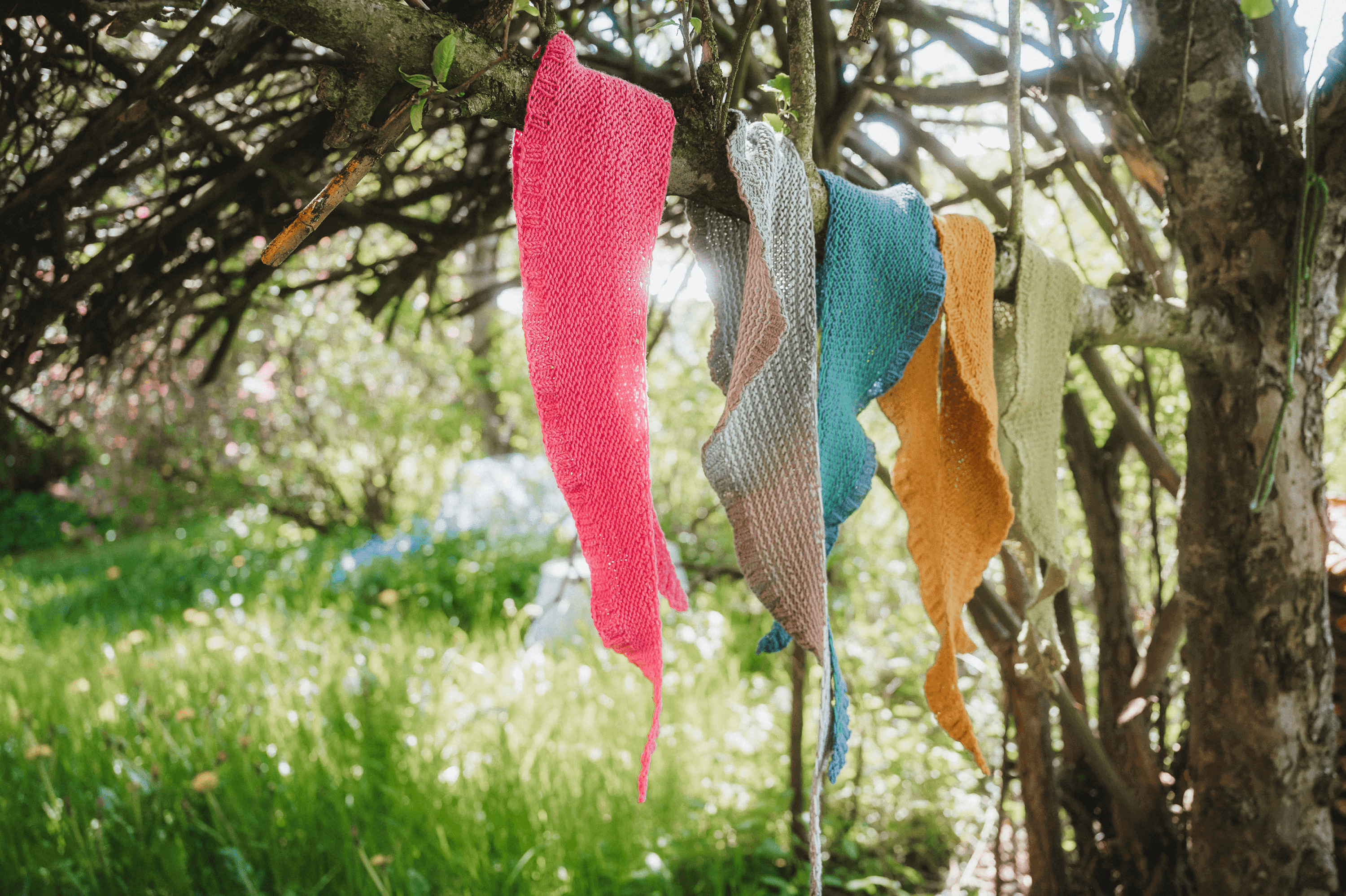Strickanleitung - Halstuch in Mondsichelform stricken Gestrickte Schals aus Finkhof Wolle in Mondsichelform hängen in verschiedenen Farben über einem Ast
