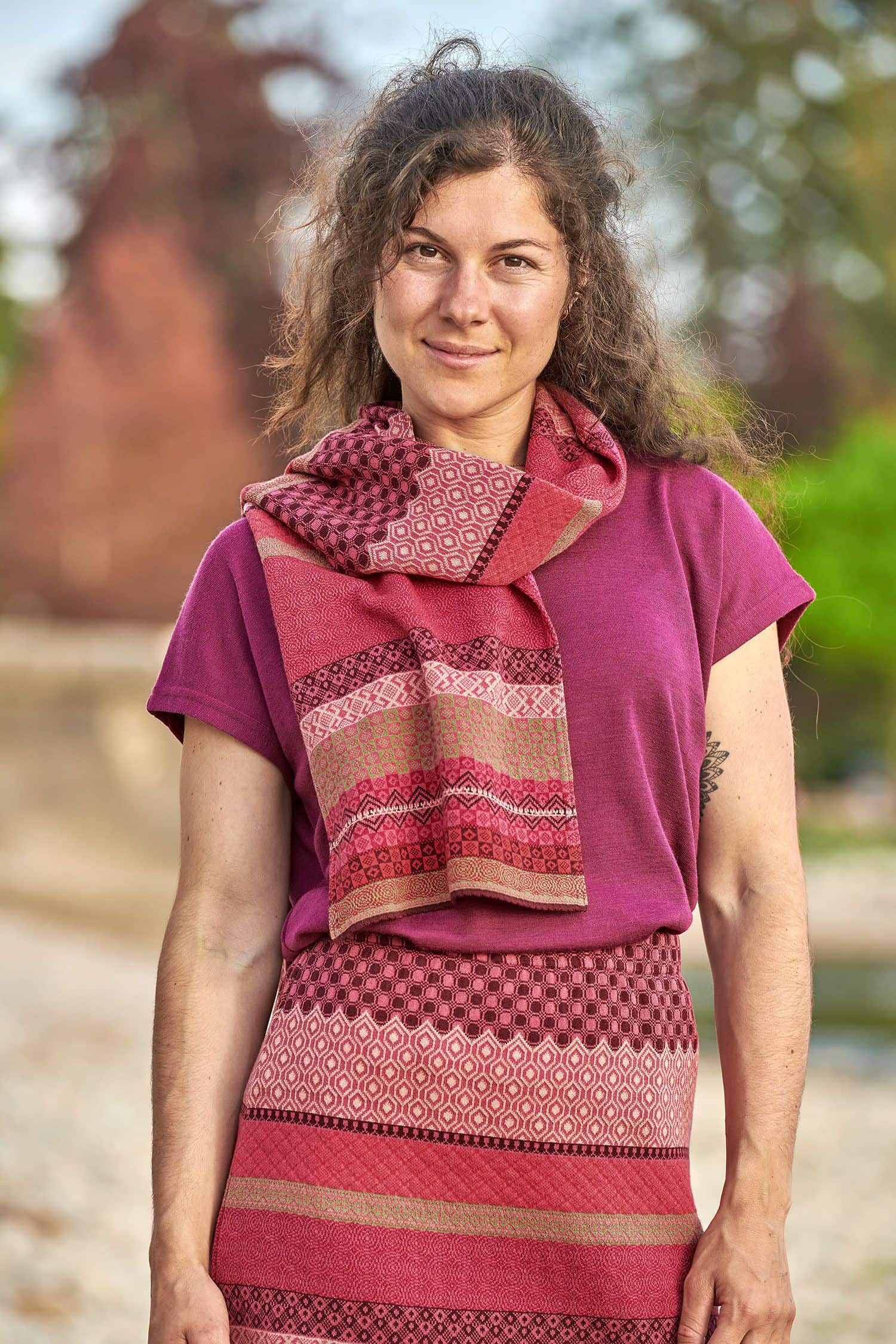 Baumwoll-Strickschal aus reiner Bio-Baumwolle Frau trägt gemusterten Strickschal aus bio Baumwolle (kbA) in beere und pink, einen Rock und ein Shirt