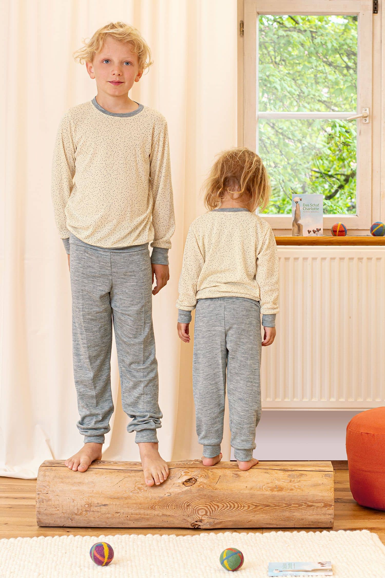 Wolle-Seide Kinder-Schlafanzughose Kinder stehen auf Holzstamm und tragen Oberteile mit Punkten und grauer Schlafanzughose aus bio Wolle (kbT) und Seide