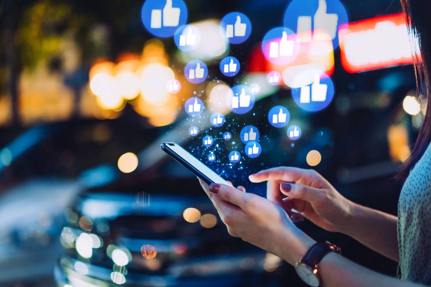 Cropped hand of young Asian woman using smartphone on social media network application on the go, viewing or giving likes in the city at night. Social media addiction concept