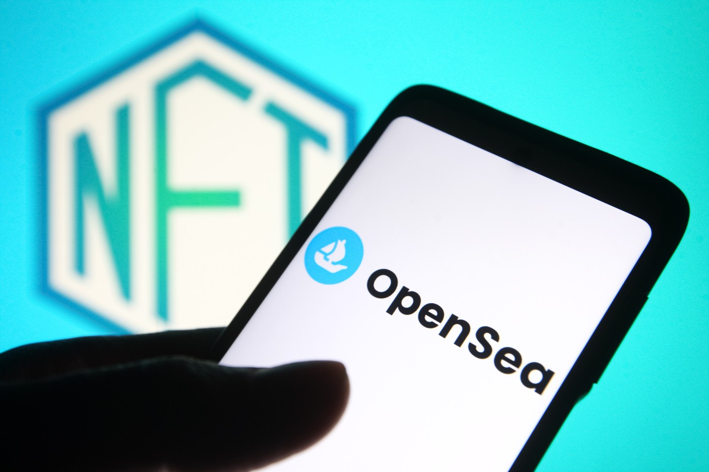 an OpenSea logo of an online marketplace for non-fungible tokens is seen on a smartphone screen and a NFT (Non-fungible token) sign in the background.