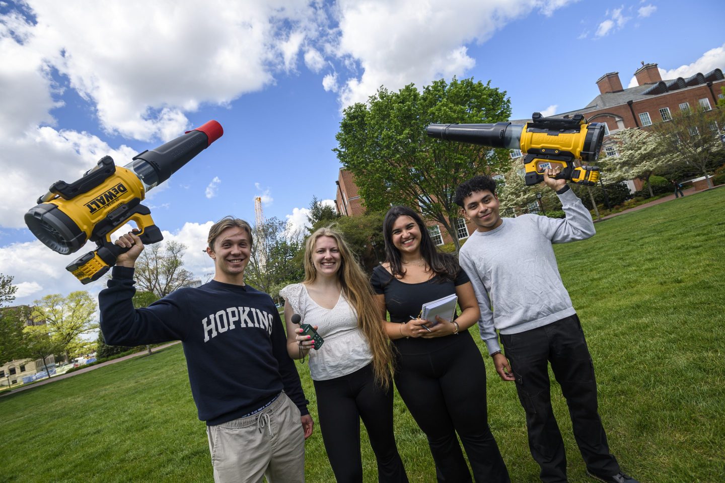Four Johns Hopkins students posing on the university's campus with two leaf blowers