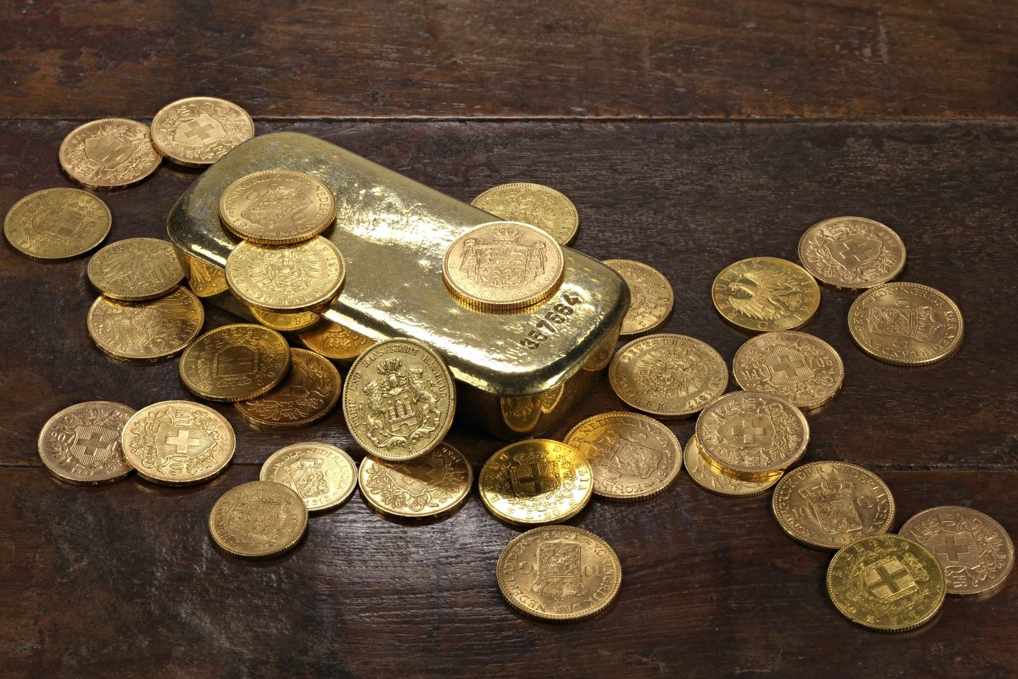 Various European circulation gold coins from the 19th/20th century around a gold bar.