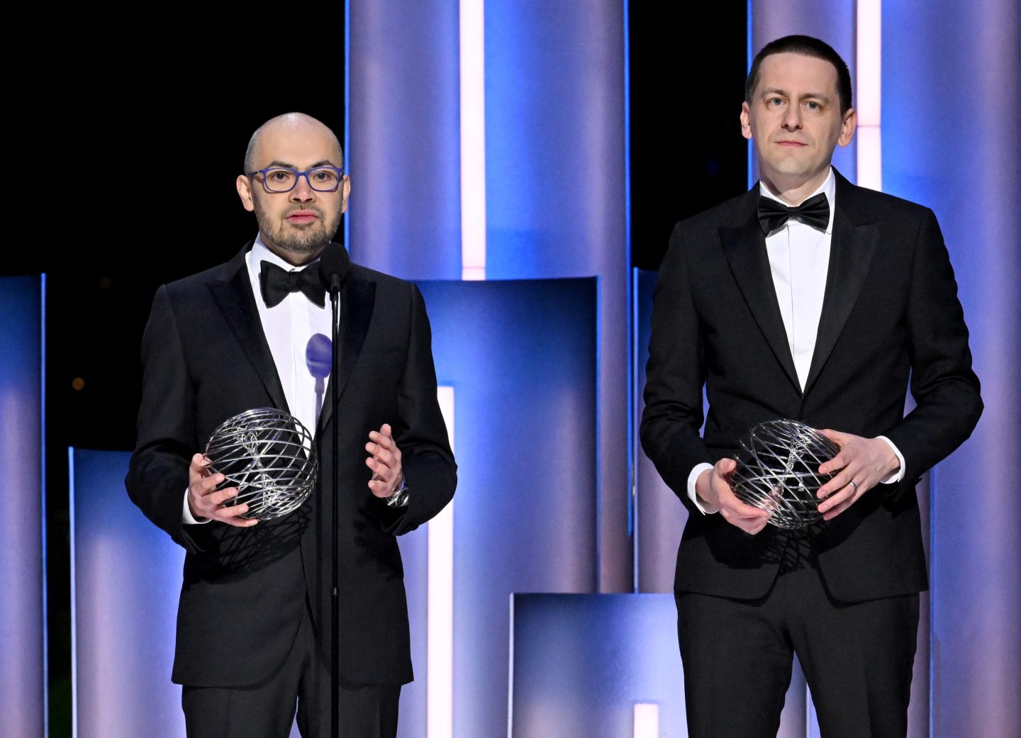 Photo of DeepMind CEO Demis Hassabis (left) and DeepMind researcher John Jumper standing in tuxedos at an award ceremony.