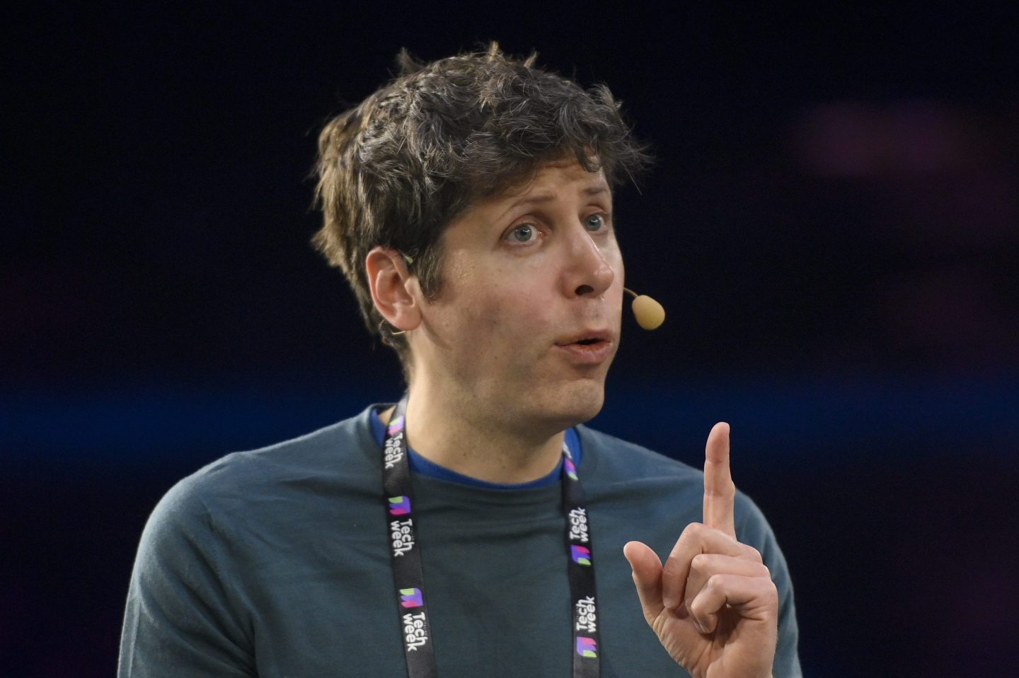 OpenAI CEO Sam Altman giving a speech and holding his index finger up.