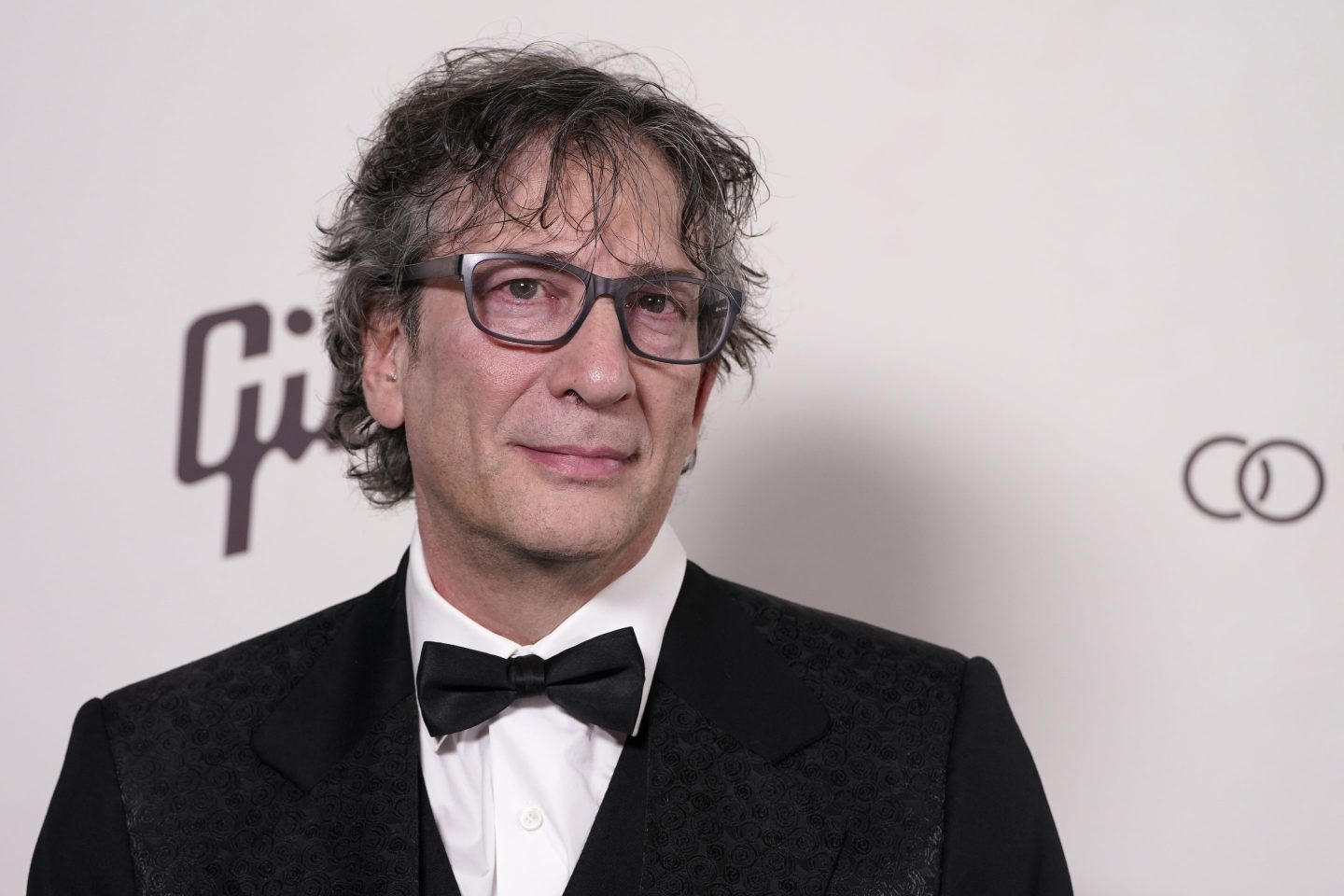 Neil Gaiman poses for the camera while wearing a tuxedo