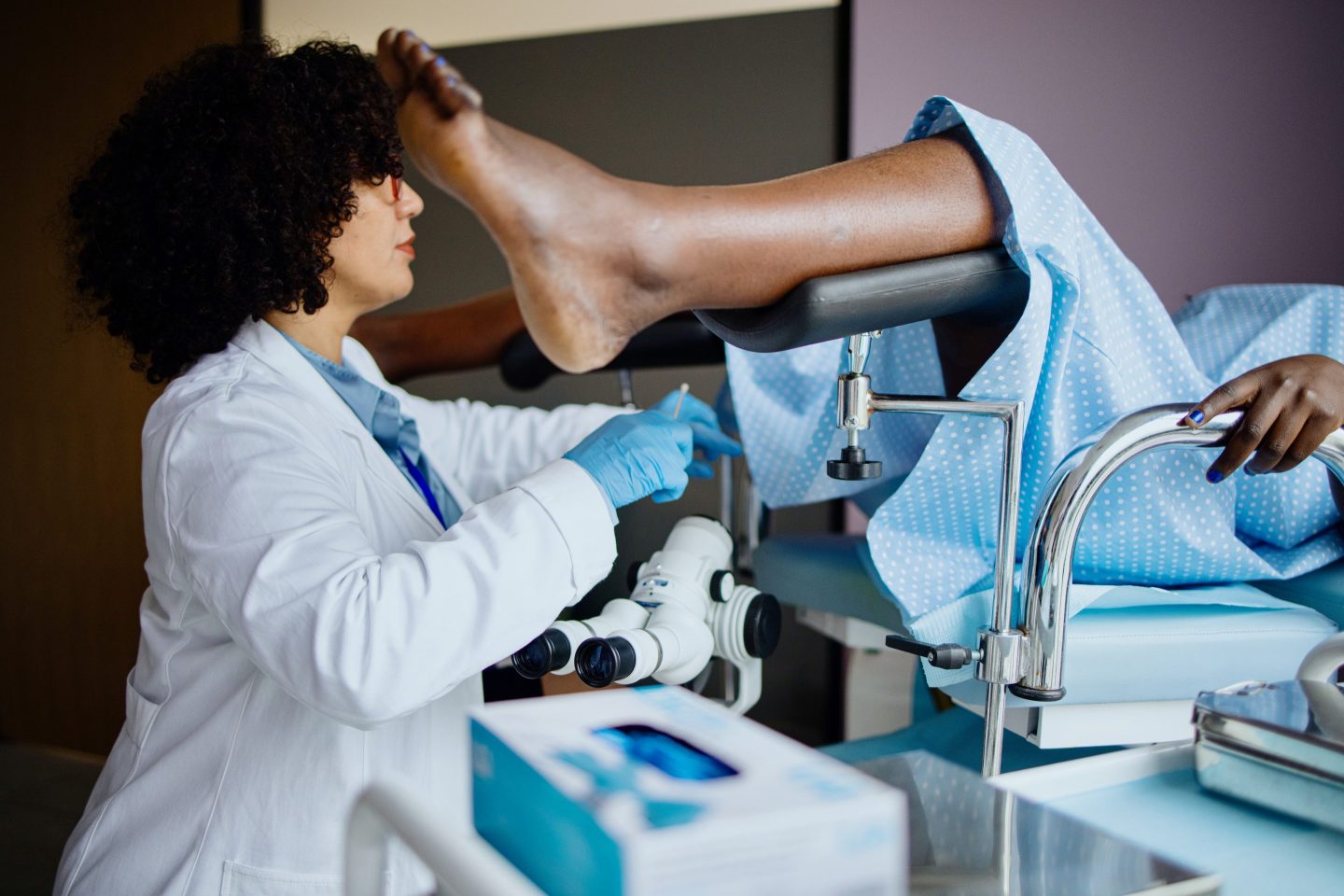 Gynecologist leaning in to bottom half of woman, legs in stirrups