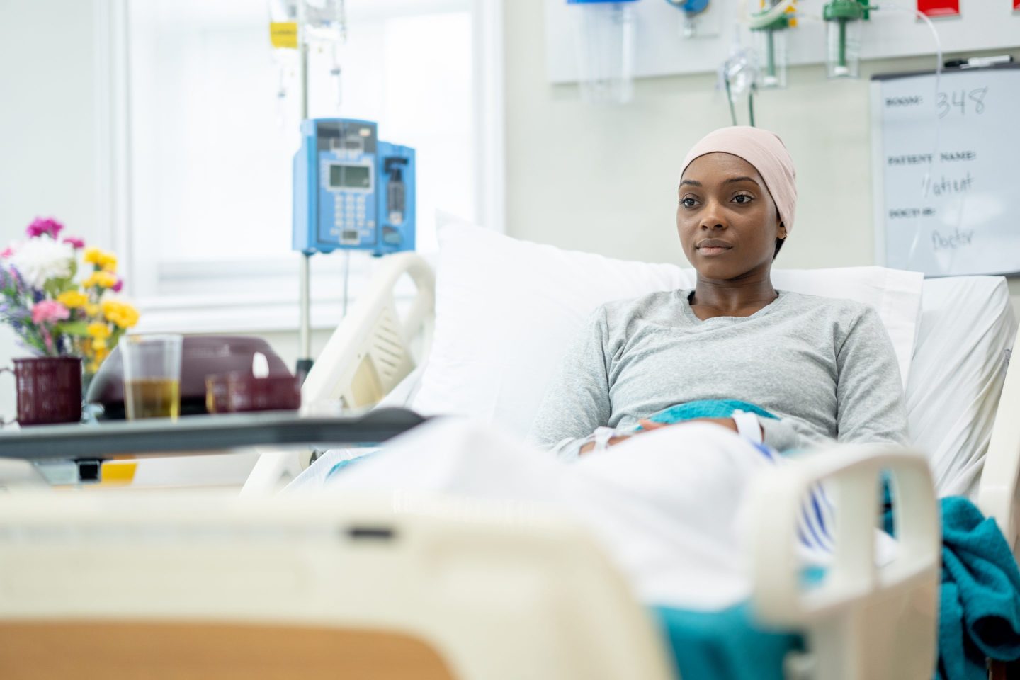 Woman in hospital bed with head wrap, suggesting cancer